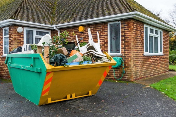 A full rubbish skip beside a house that has been filled up by the householder.